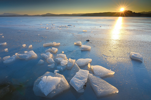 Beautiful epic ice crystal in the frozen bay. Sun rays reflection in cracks, backlight of the setting sun