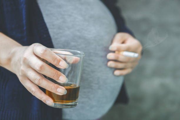 incurante incinta asiatica donna mano bere bicchiere di alcol e fumare sigaretta - abdomen addiction adult alcohol foto e immagini stock