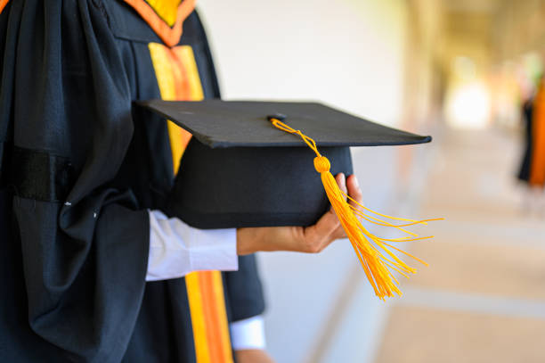 istock Graduates hold a black hat with a golden yellow tassel. 1152011714