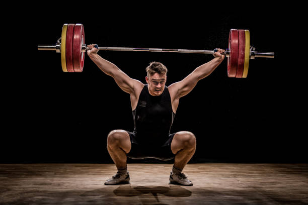 Men training with barbells Crouching body builder holding barbells performing deadlift in front of a black background. powerlifting stock pictures, royalty-free photos & images