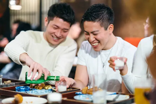 A man is pouring alcohol to his friend’s cup.