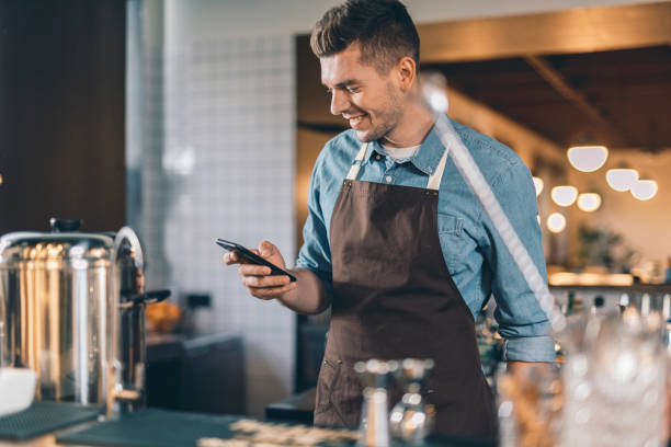 istock Positive waiter looking at the smartphone and smiling 1152014300