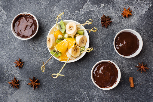 Chocolate fondue with fruit on a dark concrete background. concept summer party