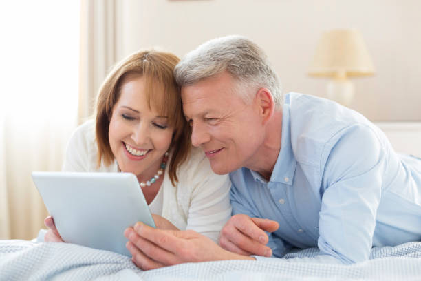 istock Smiling mature couple sharing digital tablet while lying on bed at home 1152019249