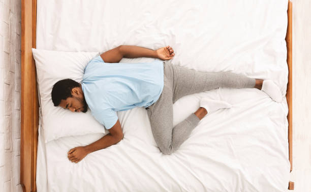 Young african-american man sleeping in bed top view Comfortable pose for sleep. Black millennial guy sleeping, lying on stomach in bed, top view man reclining stock pictures, royalty-free photos & images