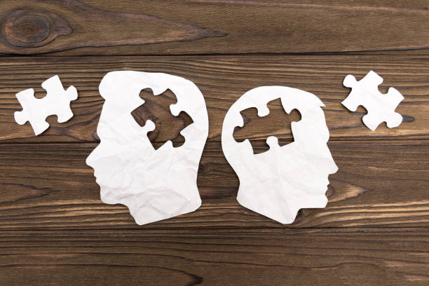 istock Two human head silhouettes with puzzles on wooden background. 1152029622