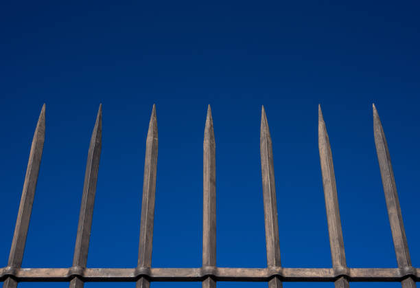 barrera de acero con barras puntiagudas contra el cielo azul - reclusion fotografías e imágenes de stock