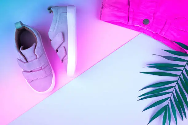 Photo of Sneakers and sprig of palm trees on a trendy neon color background, top view, summer shoes.