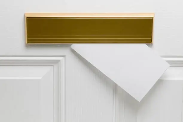 Brass letterbox on white wooden door with blank envelope