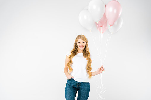 beautiful woman with hand in pocket holding white and pink air balloons on white background
