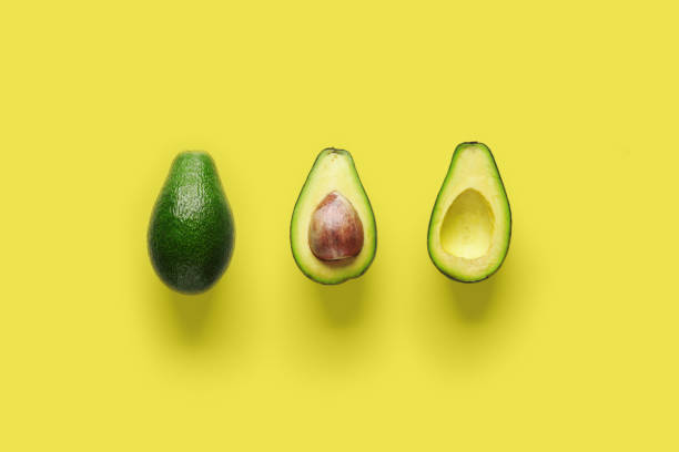 istock Whole avocado fruit and two halves in a row isolated on yellow background 1152035382