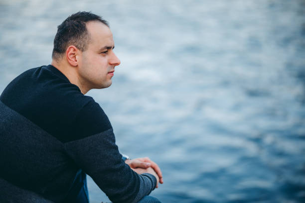 istock Man sitting alone at riverbank 1152035676