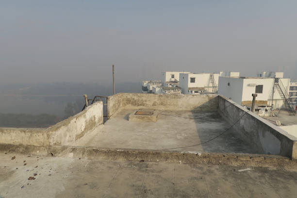 Stock photo showing tv satellite dishes on an apartment roof top with the New Delhi cityscape obscured by air pollution caused by car exhaust fumes in the background. imagen de techo de bloque de apartamento indio en nueva delhi, uttar pradesh, india, a través de agujero en la pared que muestra la contaminación del cielo nebuloso en la mañana, cielo brumoso niebla contaminada, delhi contaminación de humos de coche d