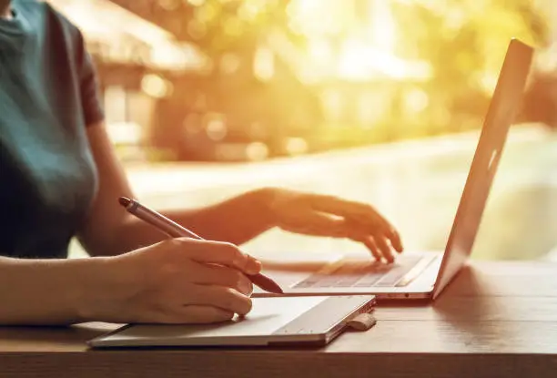 Close-up of a young female graphic designer using a digital tablet at a desk outside the office. Freelance and graphic design work concept.