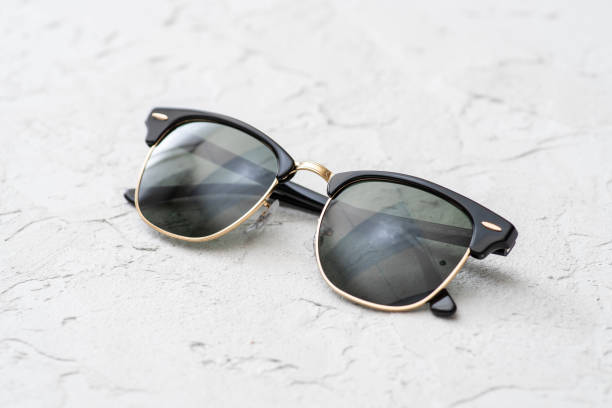 istock Black and gold frame browline sunglasses on a white concrete surface. 1152037676