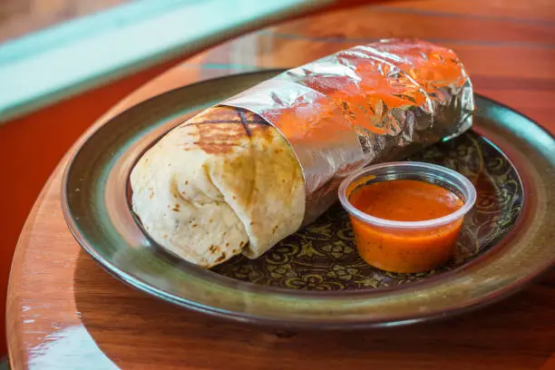 Mexican burrito with side salsa wrapped in foil.