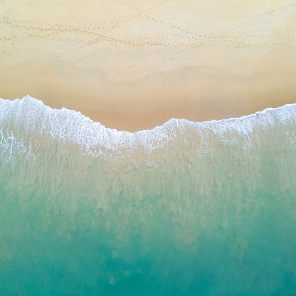 Aerial view of turquoise ocean wave reaching the coastline. Beautiful tropical beach from top view. Andaman sea in Thailand. Summer holiday vacation concept