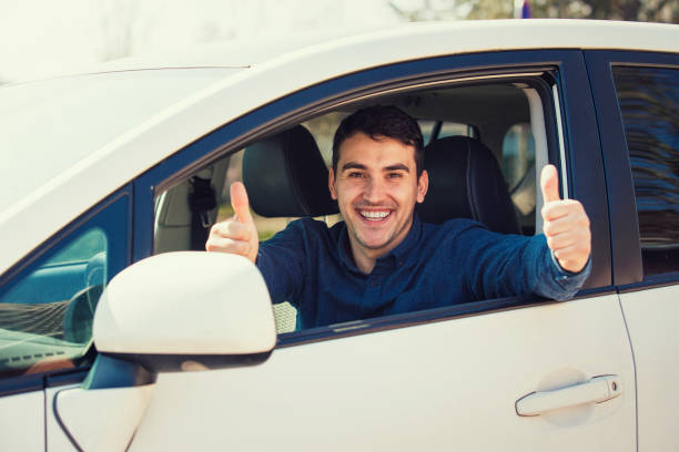 возбужденный случайный парень, сидящий за рулем автомобиля, показывая большие пальцы вверх жест, как сдал экзамен и получить водительские � - ohtani стоковые фото и изображения