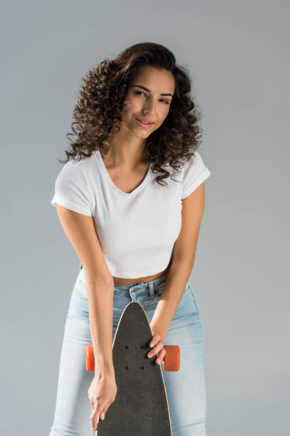 istock Curious brunette girl holding longboard isolated on grey 1152049855