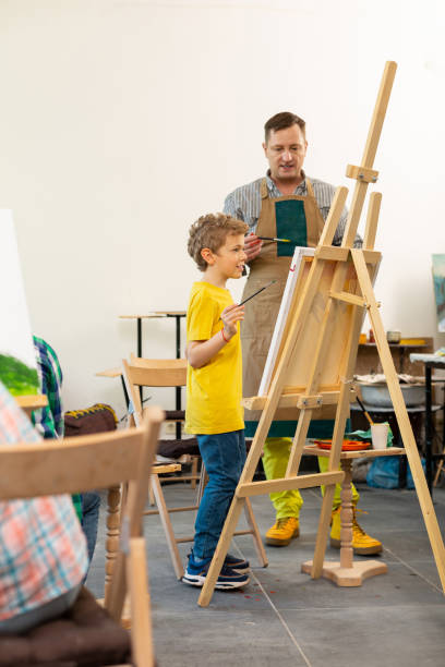 istock Art teacher helping his creative young pupil near drawing easel 1152050288