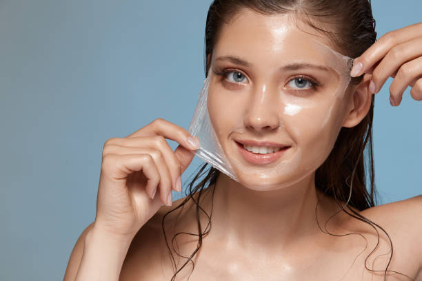woman peels-off transparent facial mask and smiling to the camera on blue stock photo