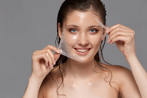 pretty woman with naked shouulders and wet hair removing facial mask isolated on grey stock photo