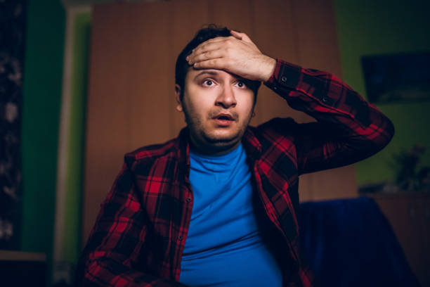 Watching tv late at night Young caucasian man on couch watching movie or live sport on TV late at night and not having a good time. excited football fan cheering for his team on tv stock pictures, royalty-free photos & images