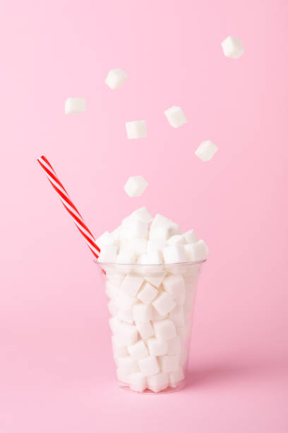 Sugar cubes falling into glass on pink background Unhealthy diet concept Sugar cubes falling into glass on pastel pink background. Unhealthy diet concept. Minimal, food levitation, side view. sugar cube stock pictures, royalty-free photos & images