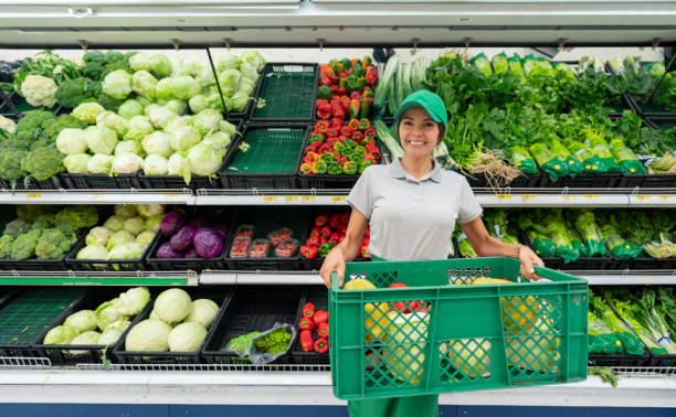 istock Cheerful woman working at a supermarket stocking refrigerated section with vegetables while facing camera smiling 1152067764