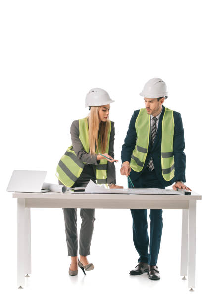 istock architects in safety vests and helmets working with blueprints and laptop, isolated on white 1152068085
