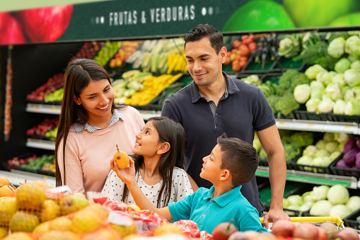 Sweet kids helping mom and dad shop for fruits at the supermarket all smiling