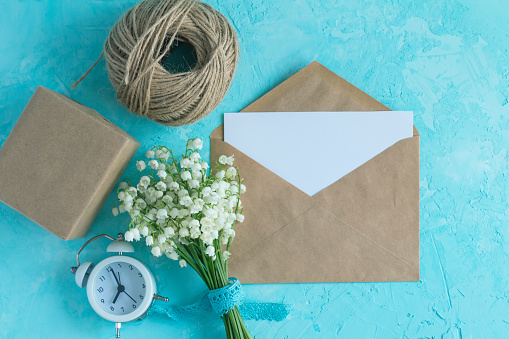 Lily of the valley bouquet and craft paper envelope on the blue surface. Top view spring flower card