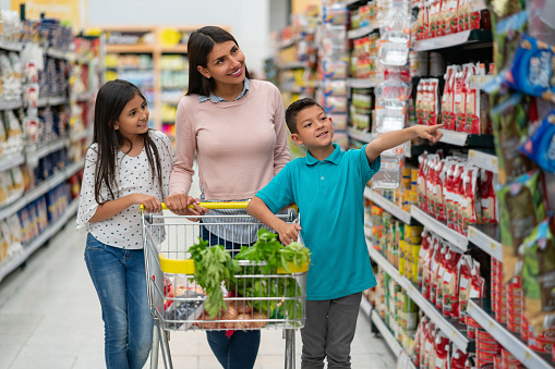Hermoso padre soltero latinoamericano con sus dos hijos en el supermercado comprando comestibles y chico apuntando a algo photo