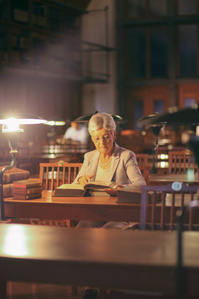 istock Senior woman reading in library at night 1152073601