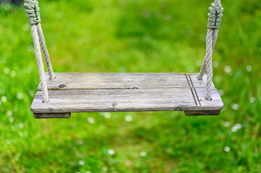 Wooden swing on ropes attached in front of a blurred background