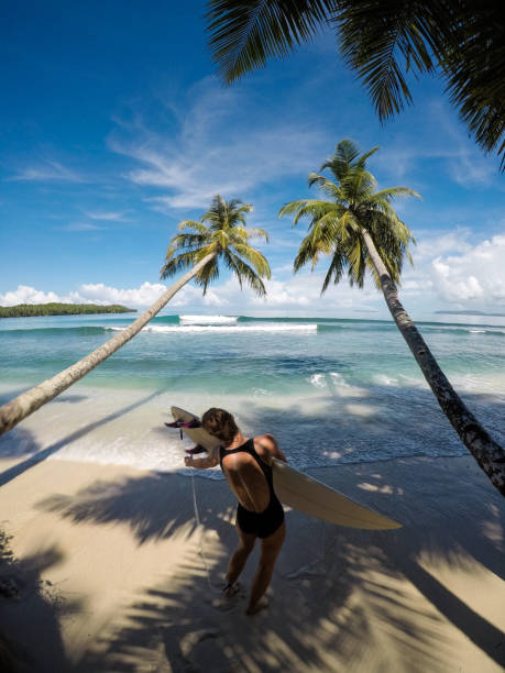 mujer con tabla de surf entre dos palmeras - mentawai islands rural scene sumatra indonesia fotografías e imágenes de stock