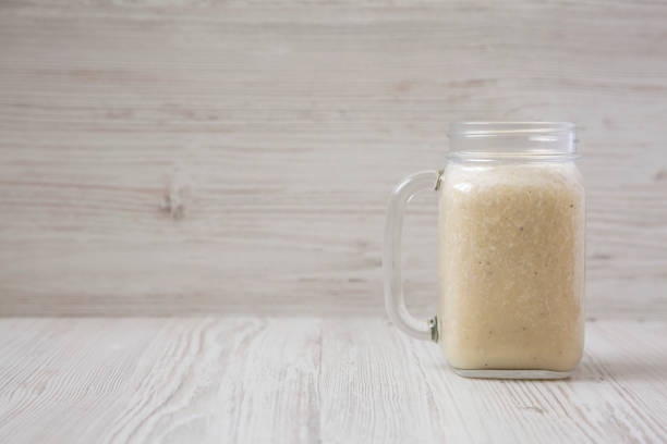 Banana smoothie in a glass jar over white wooden surface, side view. Copy space.