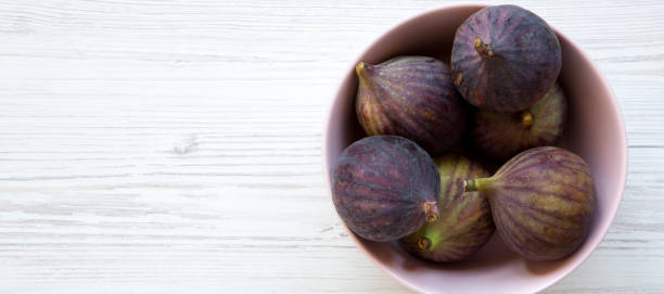 istock Fresh figs in a pink bowl over white wooden surface, overhead view. Top view, flat lay, from above. Copy space. 1152079080