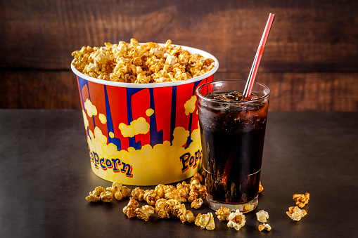 The concept of food for the cinema, for watching a movie. Cold cola drink with ice in a glass filled with popcorn. Closeup, background image. copy the text.