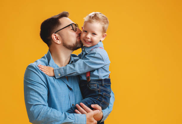 istock happy father's day! cute dad and son hugging on yellow background 1152086917