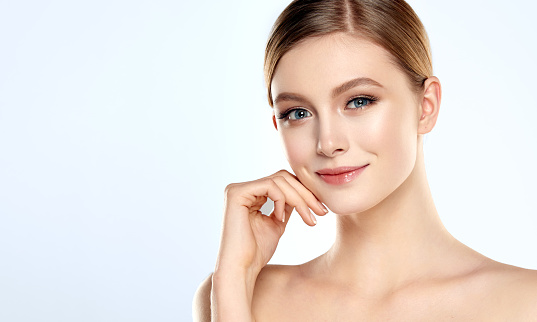 Gorgeous, young woman dressed in a soft, elegant makeup is touching the face by graceful fingers. Slender neck, bare silky shoulders and elegant gesture of hand. Facial treatment, cosmetology, beauty technologies and spa.
