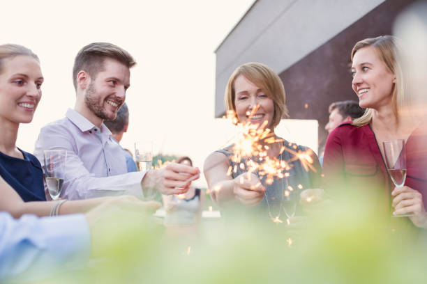 Smiling colleagues holding sparklers during party on rooftop