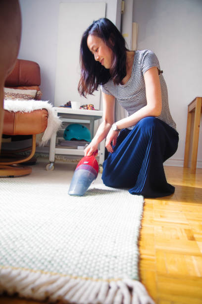 istock Young woman using a handheld mini vacuum cleaner on her carpet 1152094578
