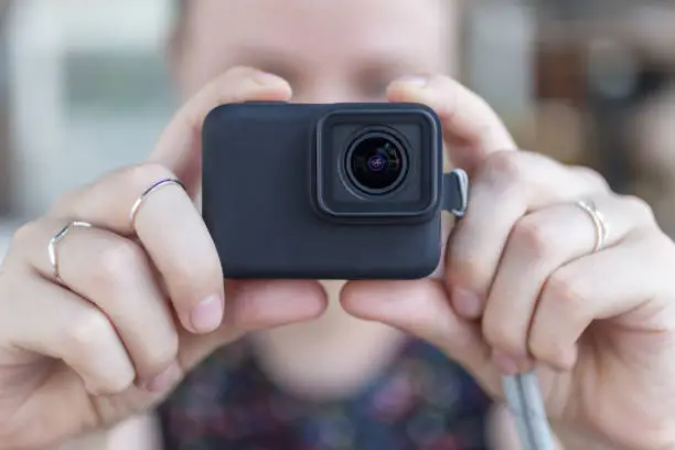 Woman's hands close up holding a small black action camera taking a video or photo