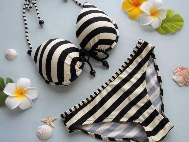 Black and white stripe bikini with plumeria flowers and seashells on light blue background.