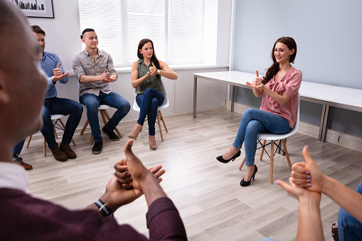 Group Of Young People Learning Deaf Gesture Sign From Woman Sitting On Chair