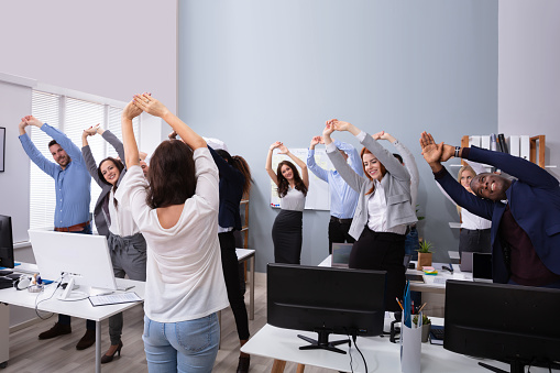 Happy Multi-ethnic Businesspeople Raising Hands Doing Stretching Exercise In Office