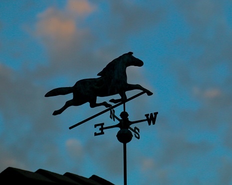 An iron weather vane shaped like a cockerel on the ridge of an old building in Woodbridge, Suffolk, Eastern England.