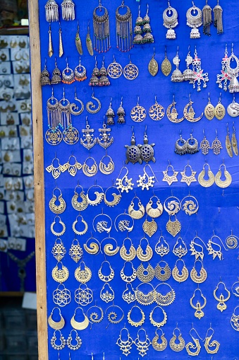 Stock photo showing homemade earrings at Indian market vendor stall against blue background, bronze metal earrings pinned to board photo in Delhi street market, Connaught Place, North India