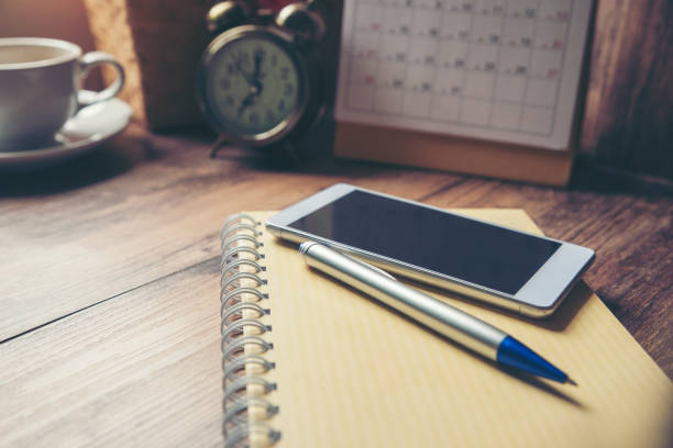 istock Diary and smartphone for planning work schedules and appointments.Desktop laptop,calendar,clock,diary,books and glasses on wooden desk,Working space at home.Urban Lifestyle concept 1152139389